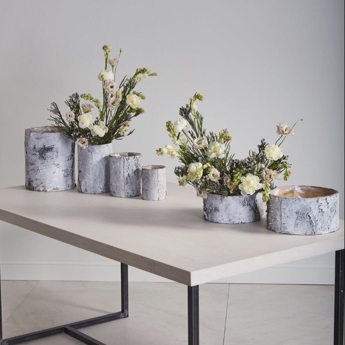 Decorative flower arrangements in rustic pots on a white table against a gray wall.