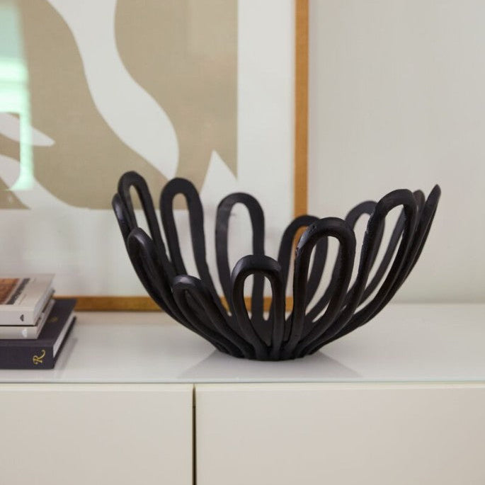Black decorative bowl on a white surface with a light-colored wall in the background