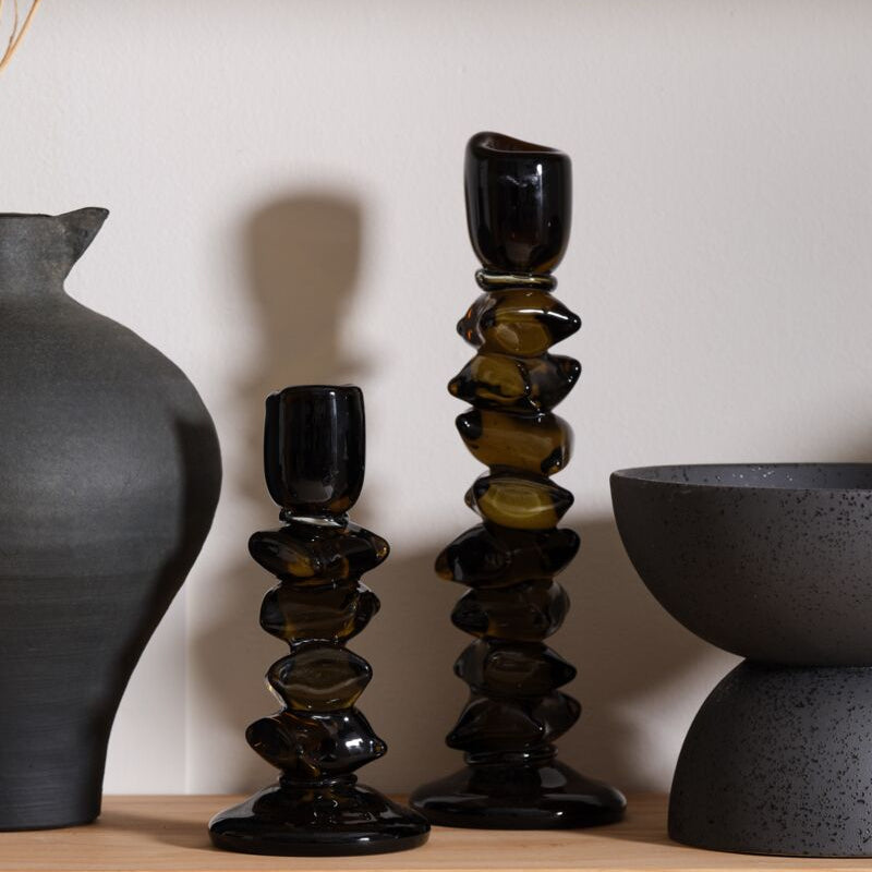 Black ceramic candle holders and vases on a wooden shelf against a neutral wall.