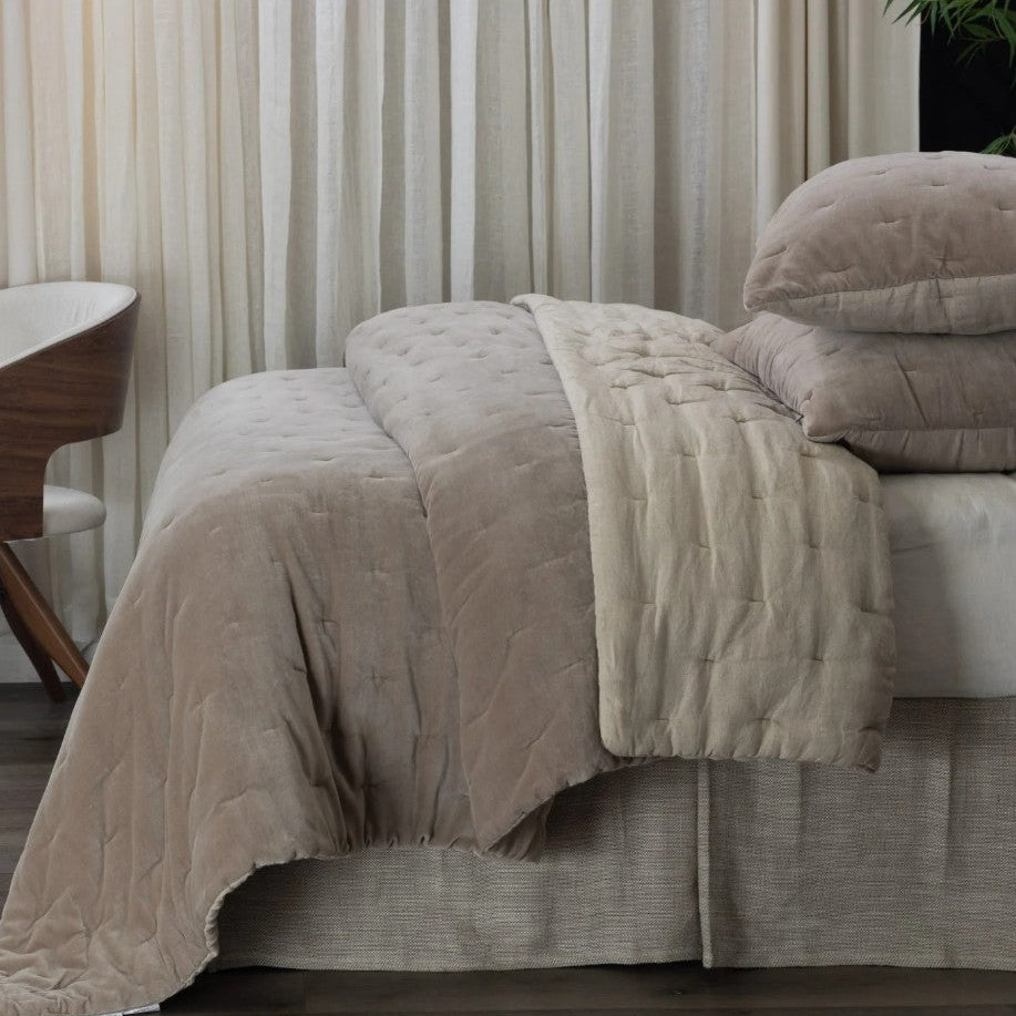 Neatly made bed with beige comforter and pillows in a bedroom setting.