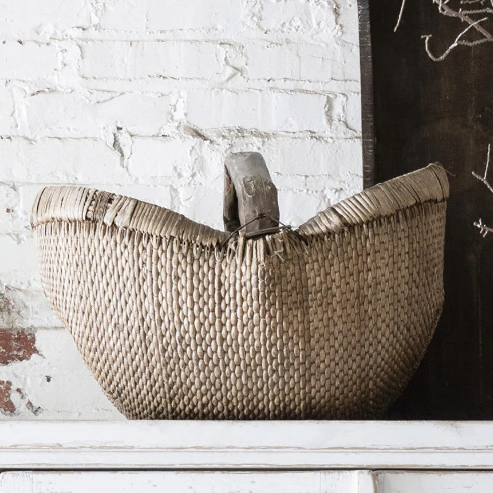Woven basket with handles on a white surface against a textured wall.
