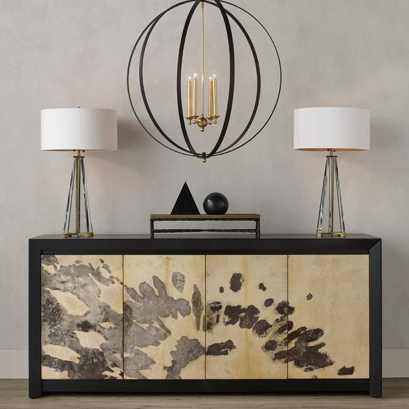 A modern black sideboard with four doors featuring abstract gold and brown leaf-like patterns, styled in a living room setting with two table lamps, a hanging black wire chandelier, and decorative objects on top.