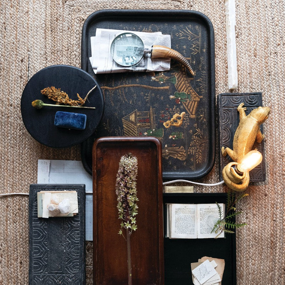 Decorative tray with various items including a magnifying glass, books, and a figurine on a textured surface.