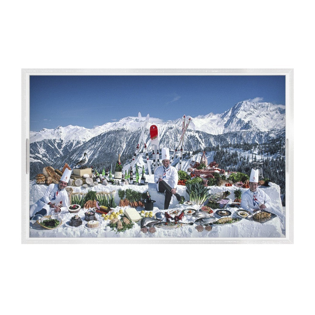 A framed photographic print depicting chefs dressed in white standing behind a massive outdoor food spread set against a backdrop of snow-covered mountains under a clear blue sky.