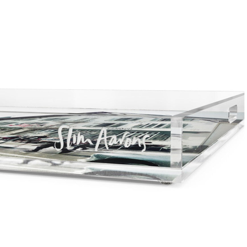 A clear acrylic rectangular tray with a handle, featuring the name 'Slim Aarons' printed in white script on the side, set against a plain white background.