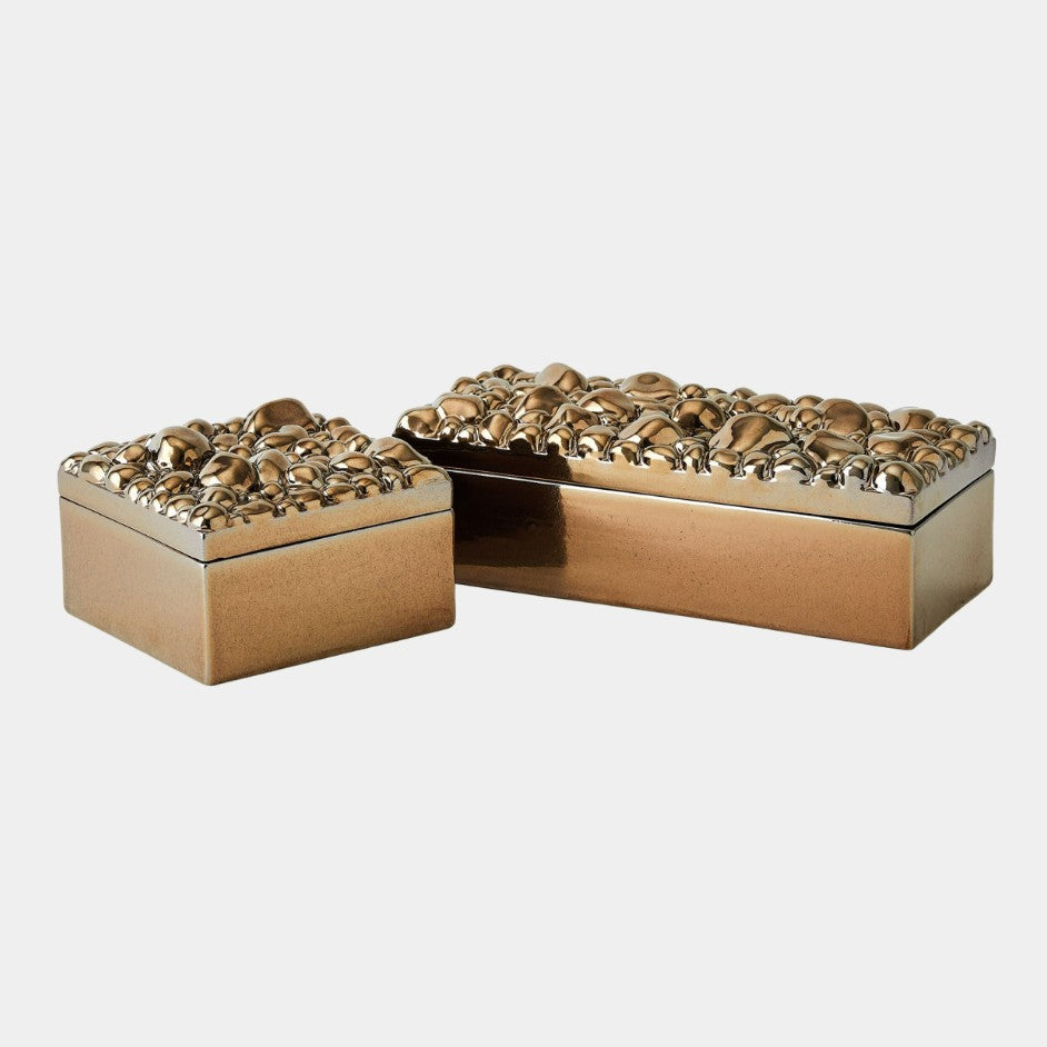Two gold decorative boxes with intricate designs on a light gray background