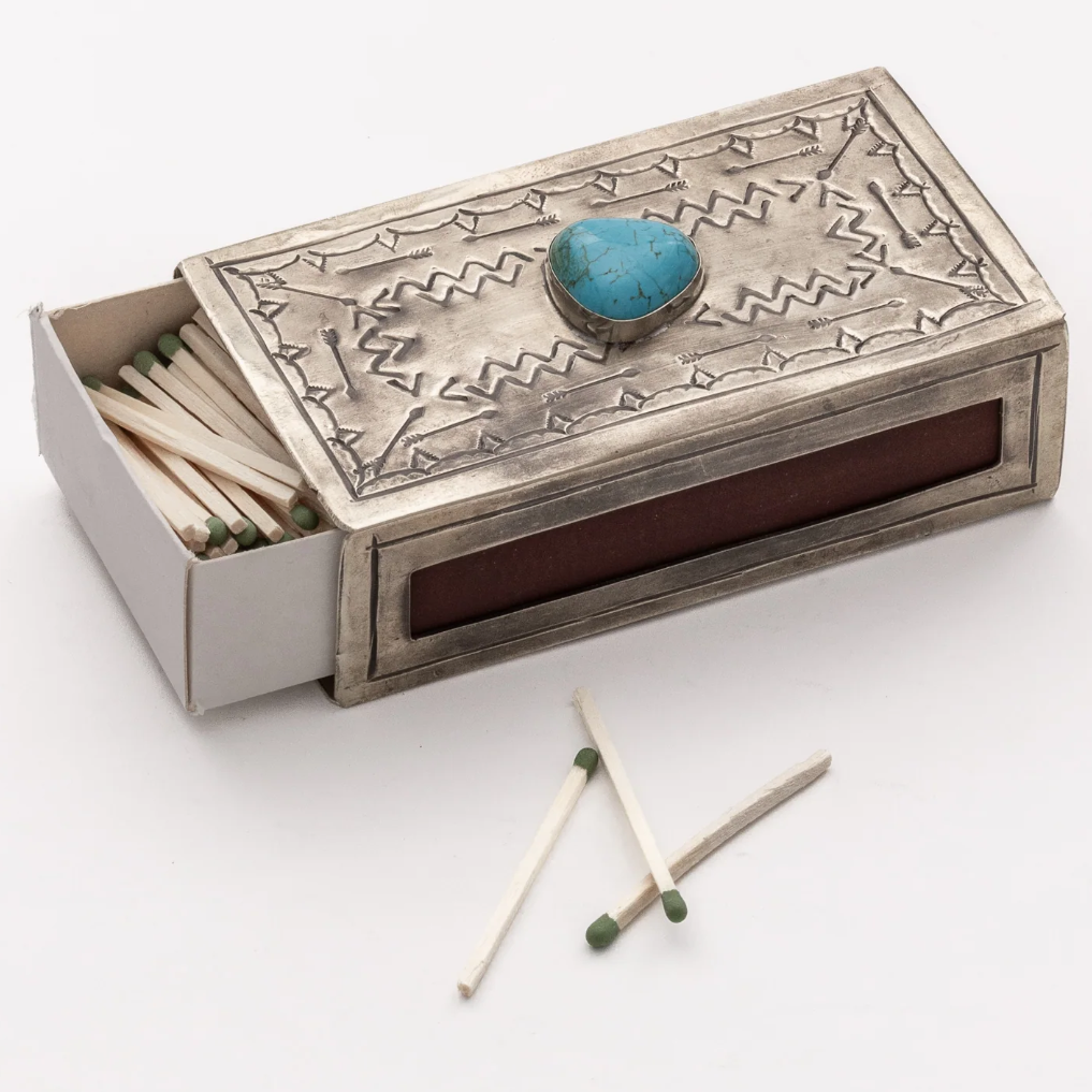 An ornate silver-toned matchbox with a turquoise stone accent on the lid, shown open with matches inside and two matches placed outside on a clean white background.