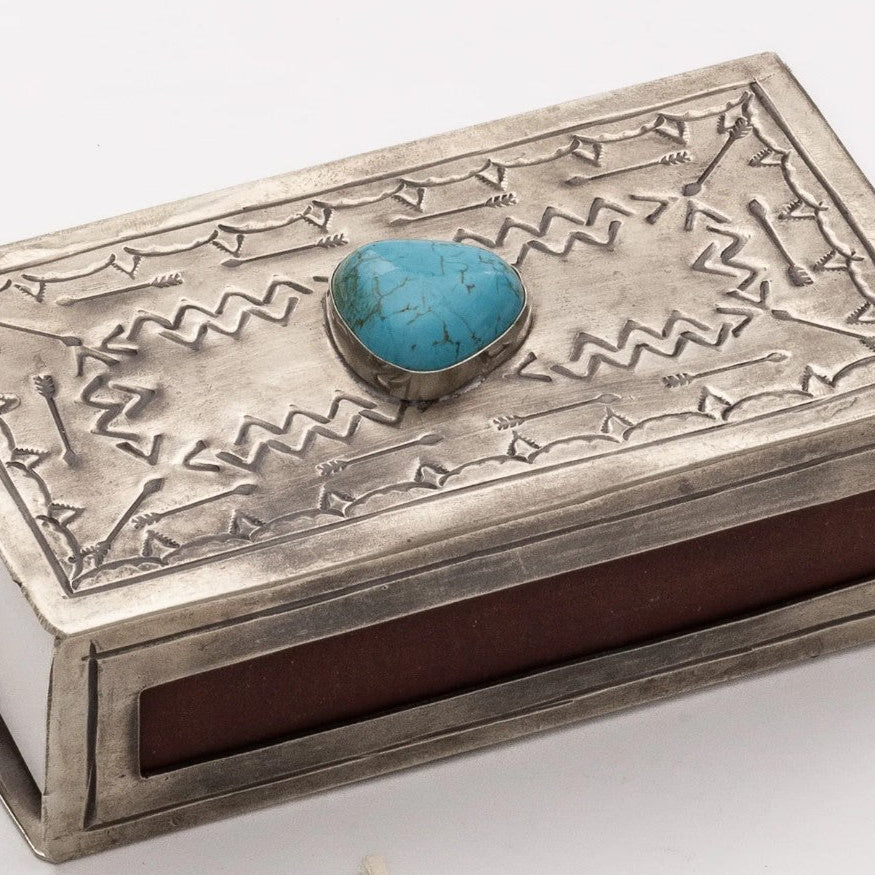 A sterling silver matchbox-style decorative box with engraved geometric patterns, featuring a turquoise stone inlay on the lid and a dark reddish-brown interior, shown on a white background.