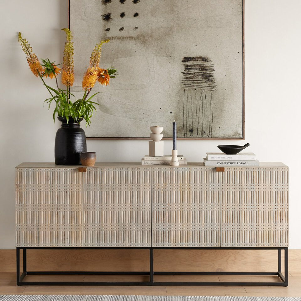Decorative console table with a vase of flowers, books, and a framed abstract painting in a room.