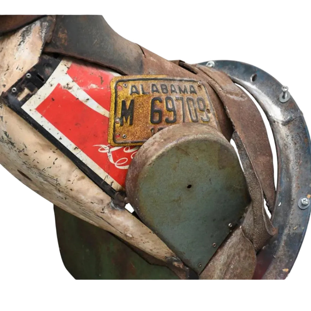 A close-up of a rustic metal and wood object featuring a vintage Alabama license plate reading 'M 69703', a red and white flag, and a curved metal piece, shown against a white background.