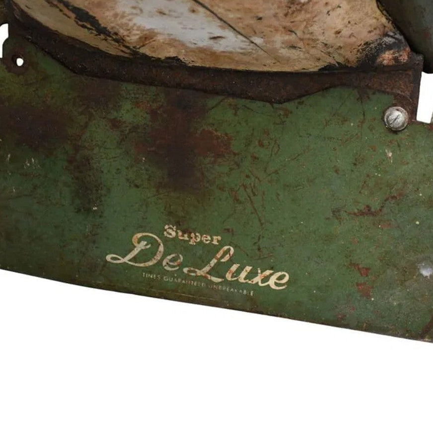 Close-up of a vintage green metal blade or guard with rusted areas and the words 'Super De Luxe' printed in gold on a white background.