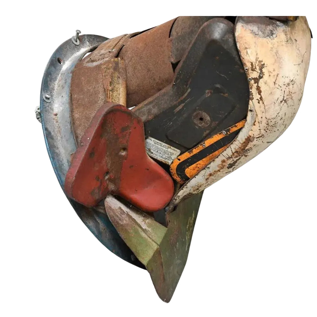 A close-up of a used industrial or agricultural attachment component, featuring a rusted brown metal body, a red plastic blade, a black plastic housing, and a weathered off-white outer casing, isolated on a white background.