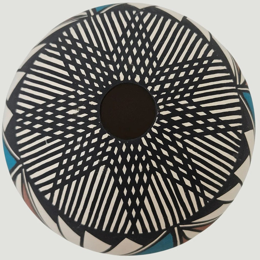 A round decorative bowl with a geometric pattern of black radiating lines on an off-white background, featuring a solid black center and small blue accents near the rim.