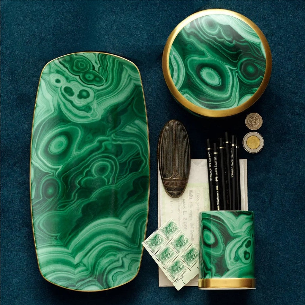 A luxury stationery and desk accessory set featuring a green malachite stone pattern with gold trim, including a tray, circular box, notebook, pencil holder, and stamp sheets, arranged on a dark blue textured background.