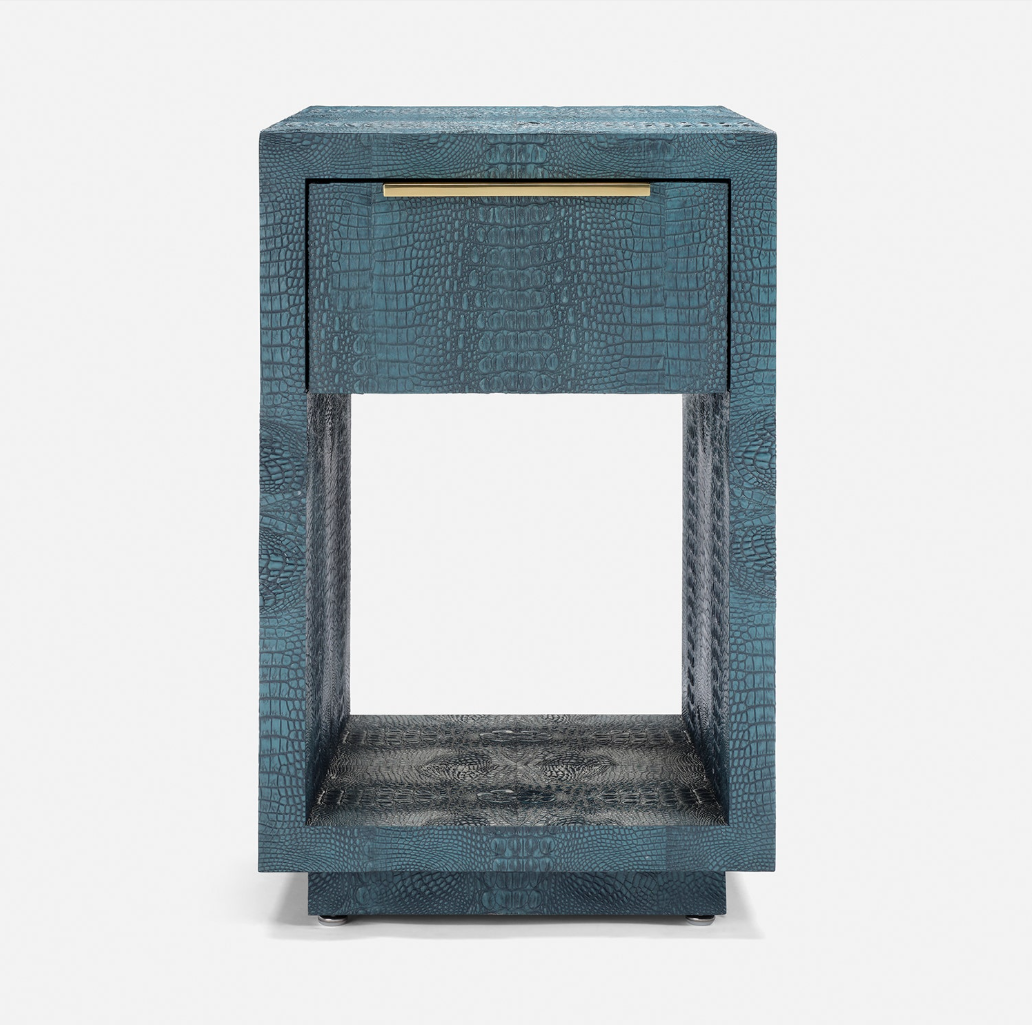 A modern side table with a textured blue-green crocodile skin finish, featuring a single drawer with a gold pull handle and an open lower shelf, set against a plain white background.