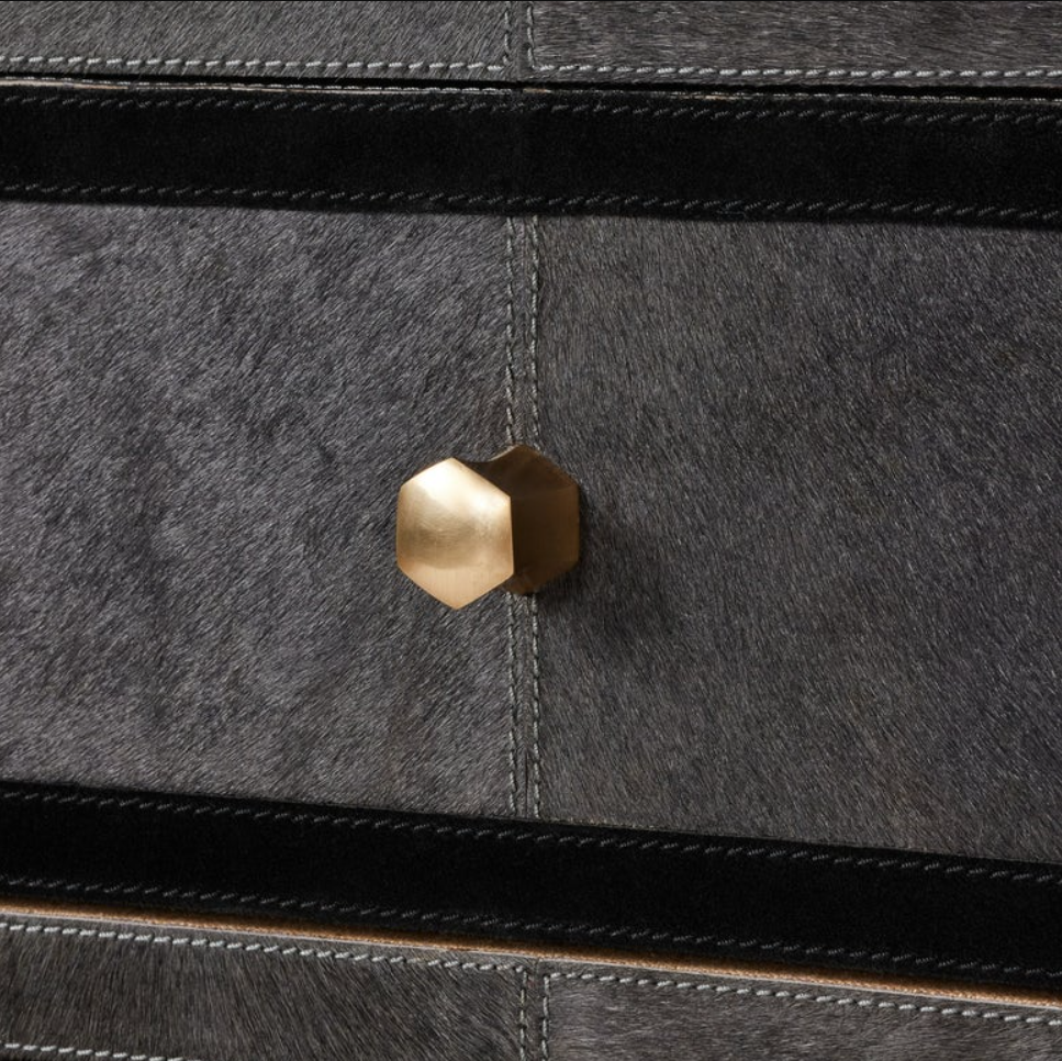 Close-up of a dark gray textured cabinet or drawer front with black stitched trim and a faceted metallic gold hexagonal knob at the center.