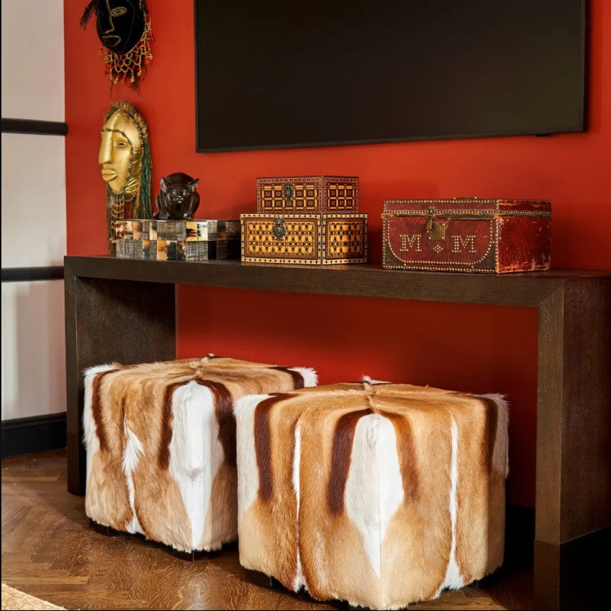 Decorative room with fur ottomans, a console table with trinkets, and a red wall.