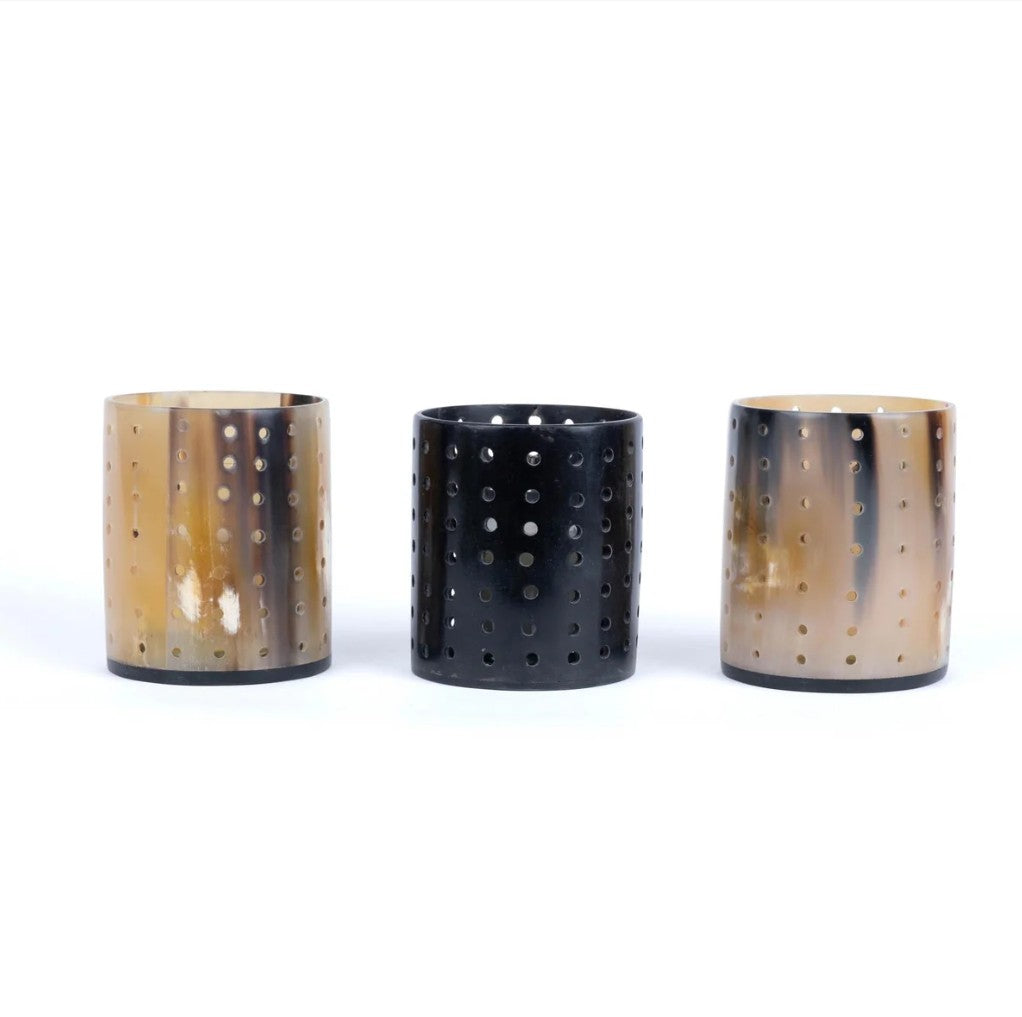 Three cylindrical cow horn tea light votives with perforated designs on a white background