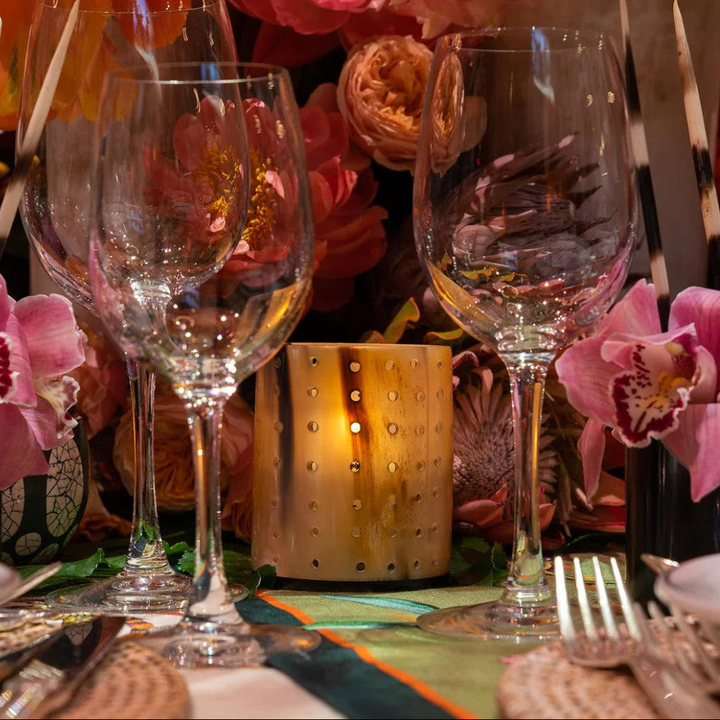 Decorative table setting with wine glasses, flowers, and cow horn votive.