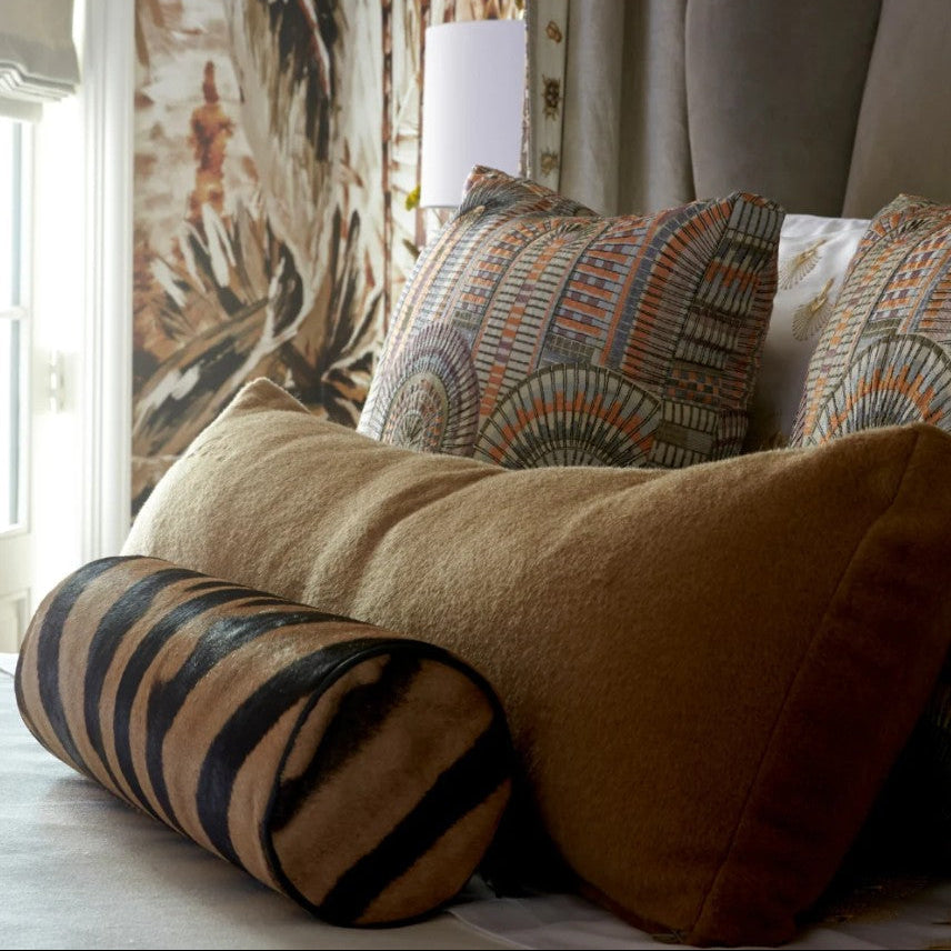 Decorative pillows on a bed with a zebra-patterned cylindrical pillow.