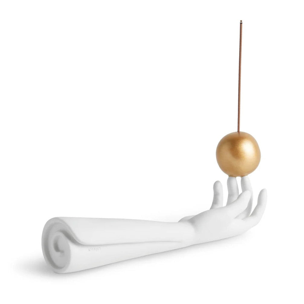 A white sculptural hand sculpture holding a thin vertical rod with a metallic gold sphere balanced on its fingertips, set against a plain white background.