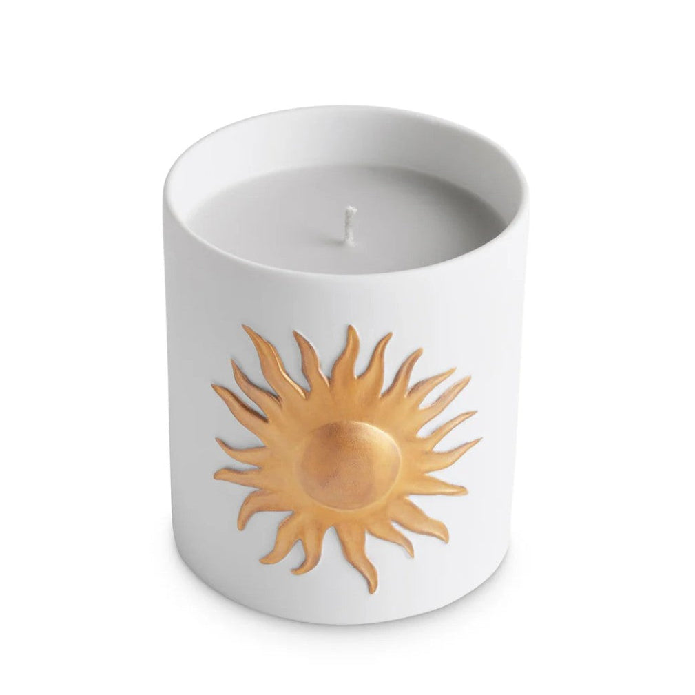 A white ceramic candle jar with a textured gold sun design on the front, set against a plain white background.