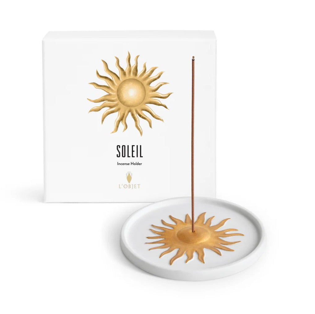 L'Osuit Soleil incense holder set, featuring a white ceramic dish with a gold sunburst design, a single incense stick, and its white packaging box with a gold sunburst logo.