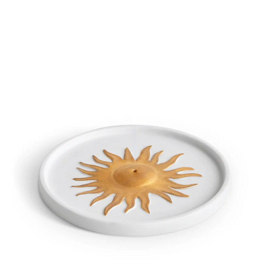 A white ceramic candle holder featuring a raised gold sun emblem in the center, shown on a plain white background.