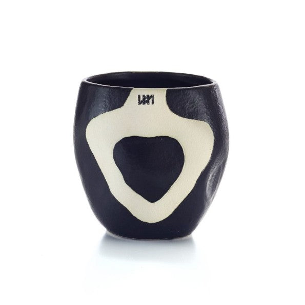 A black ceramic cup with a cream-colored abstract heart-shaped pattern on the front, photographed on a clean white background.