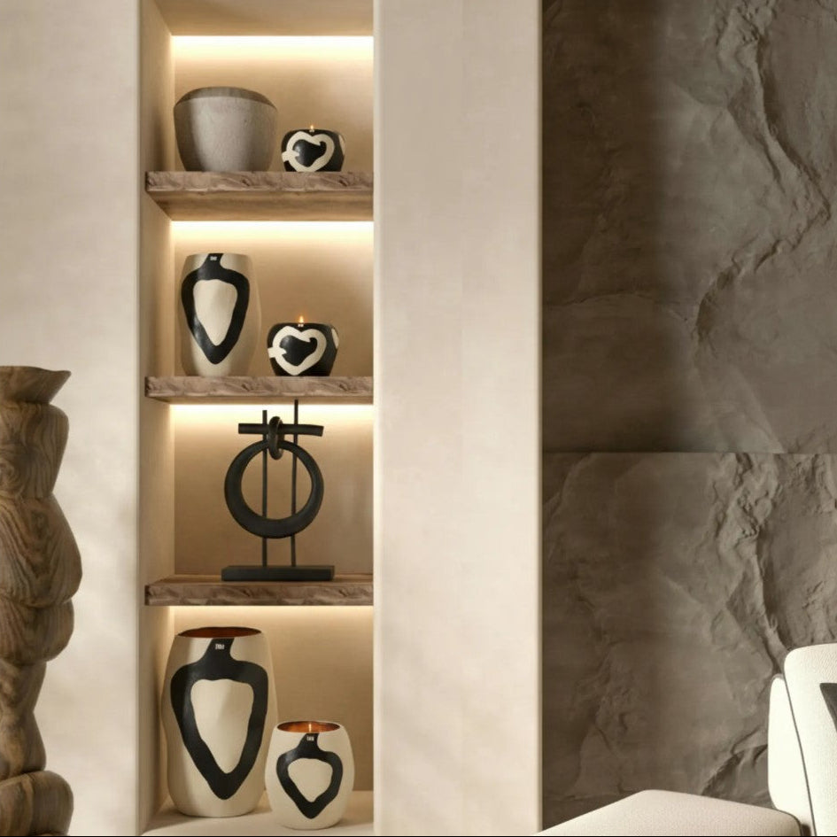 A set of modern black and white ceramic vases and sculptural decor pieces displayed on built-in wooden shelves with warm LED lighting, set against a textured beige plaster wall and a dark stone accent wall.