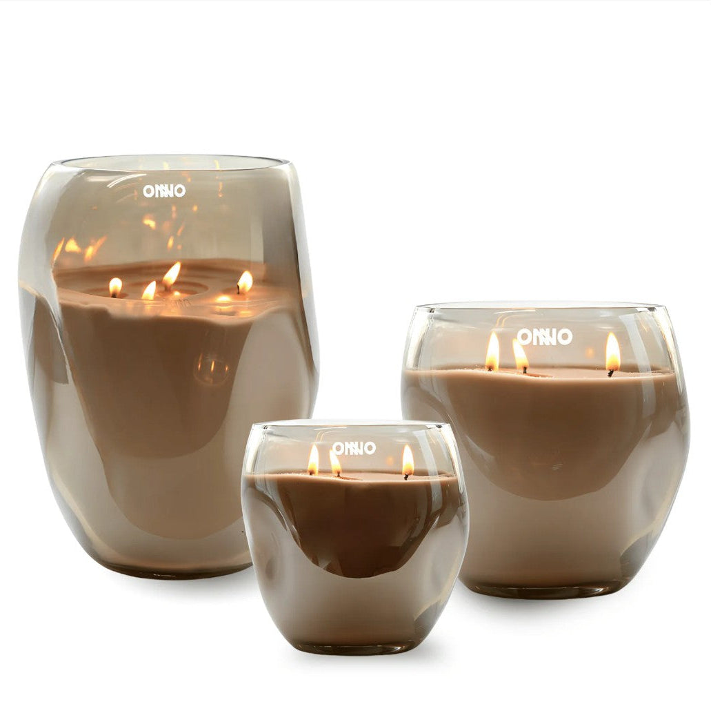Three O'NIO glass jar candles in different sizes, filled with brown wax and lit with visible flames, set against a white background with black side bars.