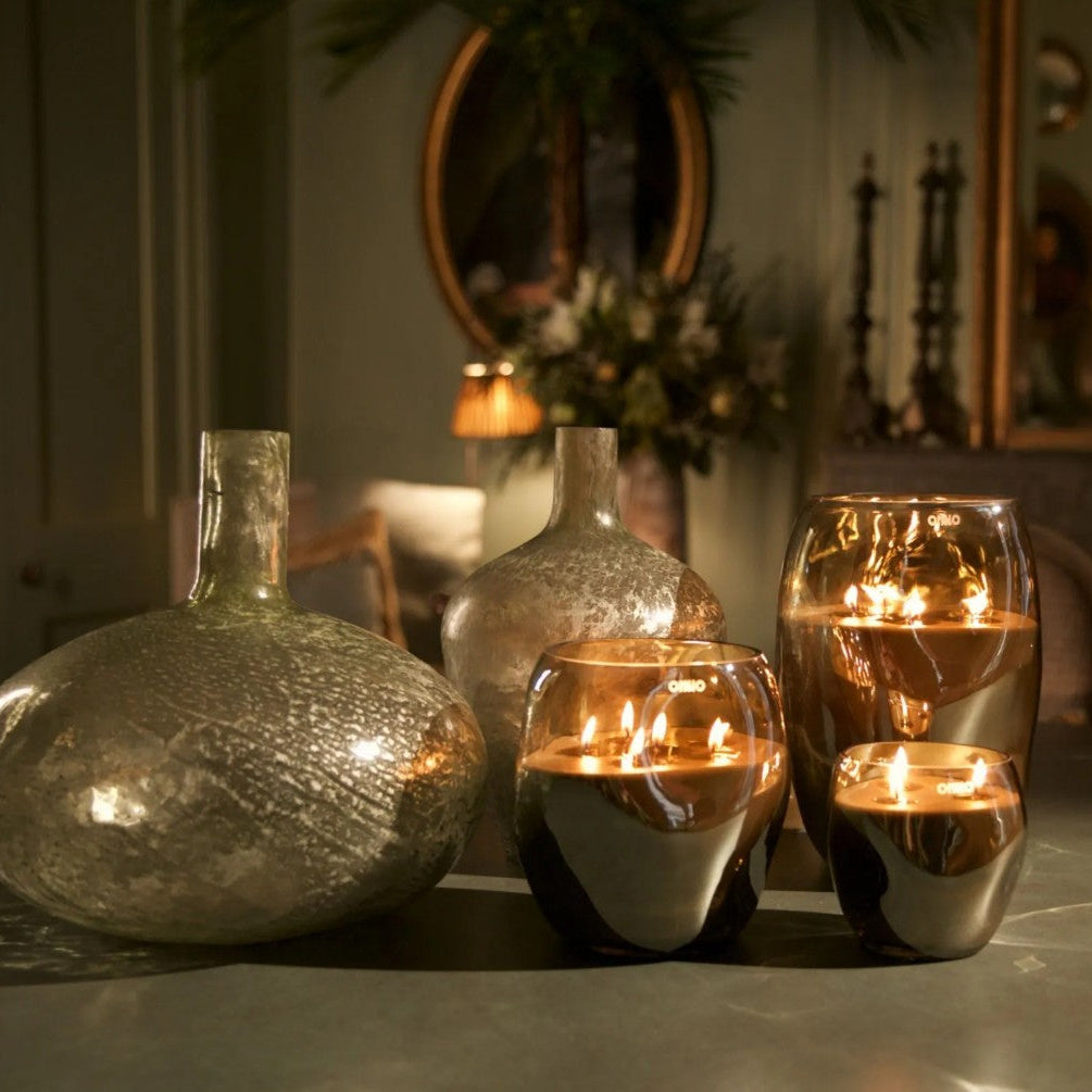 A set of decorative glass vases and candle holders with lit candles, arranged on a tabletop in a softly lit interior setting.