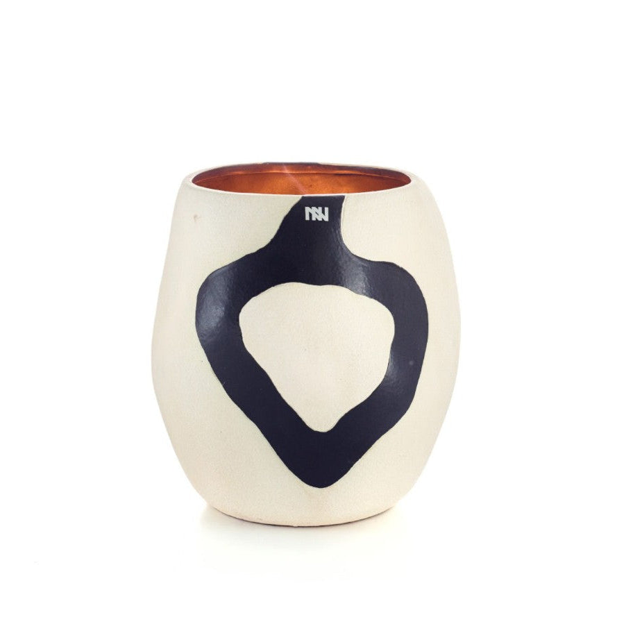 A ceramic candle holder with a rounded, organic silhouette. The body is cream-colored with a large, bold black heart-shaped graphic on the front, and a warm copper-orange interior visible at the top.