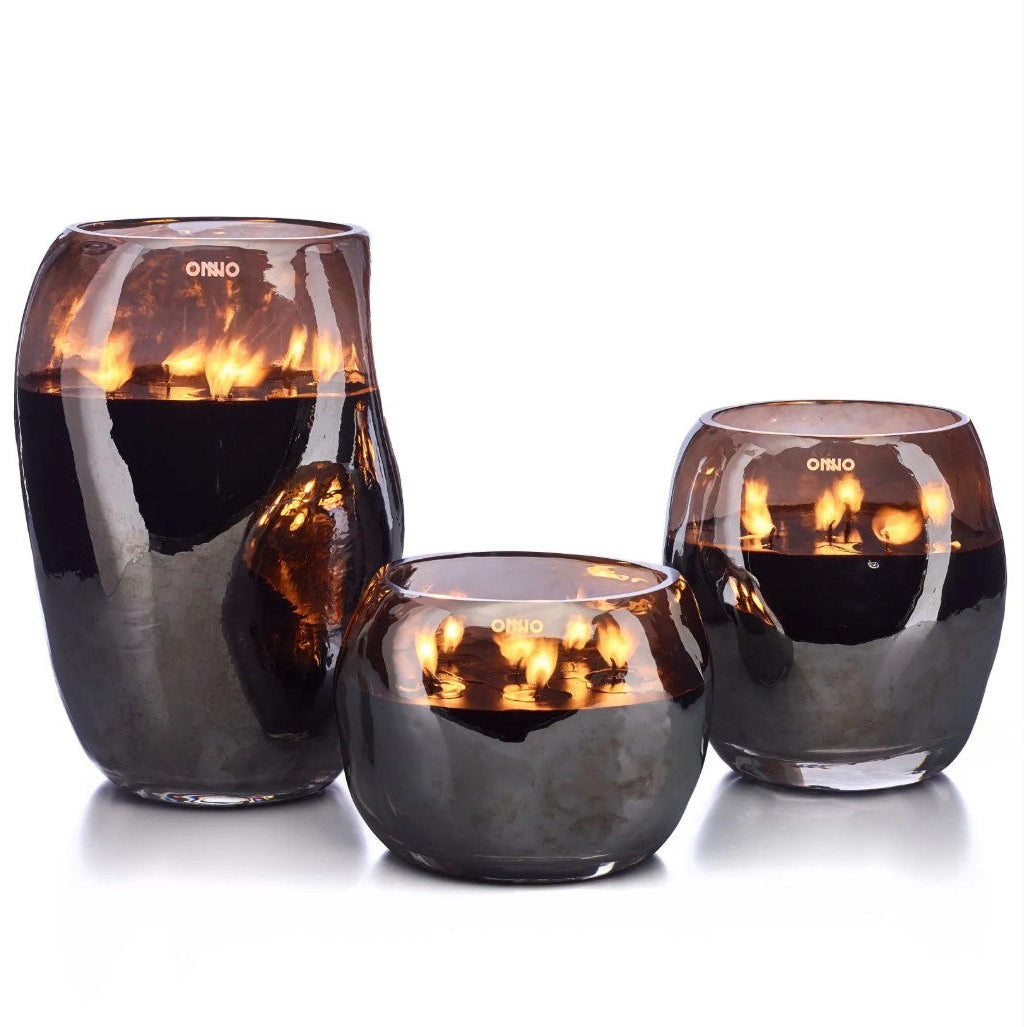 Three amber glass candle holders of different sizes, each containing a lit candle, displayed on a white background with black side bars.