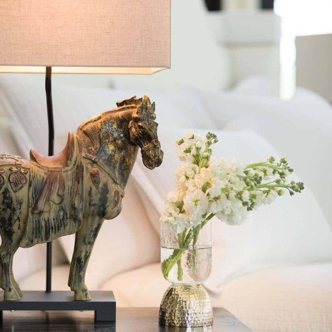Decorative horse figure and vase with flowers on a black dresser.