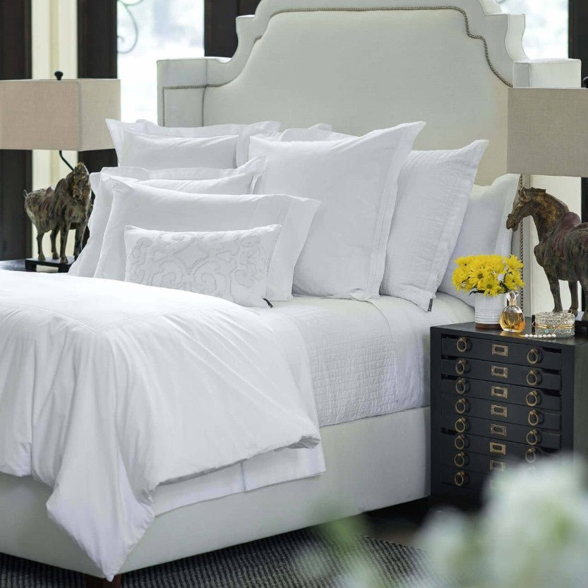 Neatly made bed with white bedding and pillows in a bedroom setting.