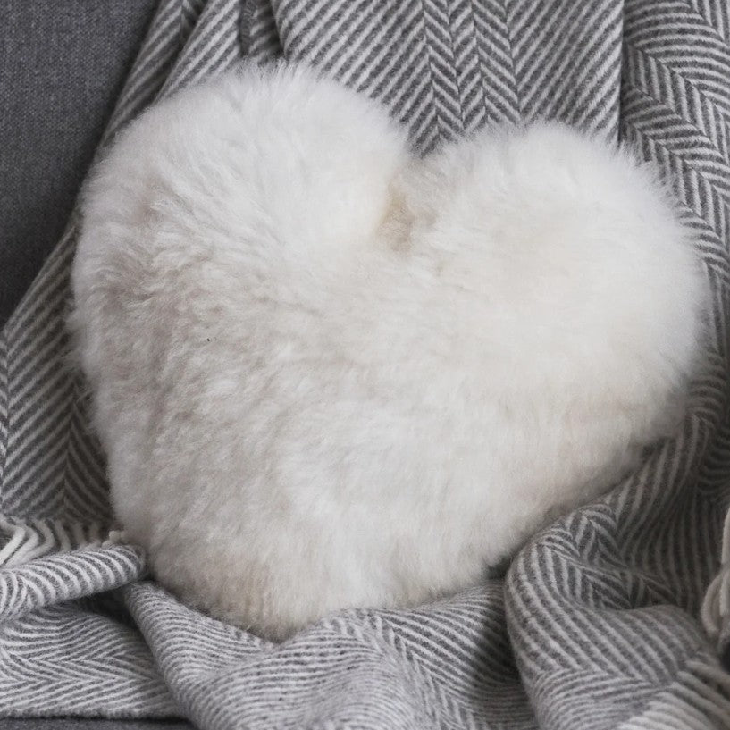 White fluffy heart-shaped pillow on a textured gray blanket