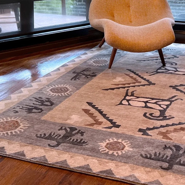 A rectangular area rug with a Southwestern geometric pattern in beige, brown, and gray, styled on a dark wood floor in a modern living room setting with a mid-century modern chair and a side table.