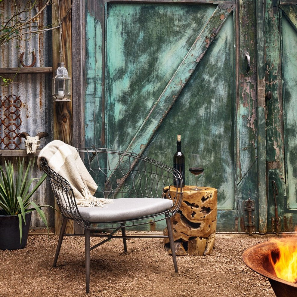Outdoor setting with a chair, bottle, and glass against a rustic metal gate.