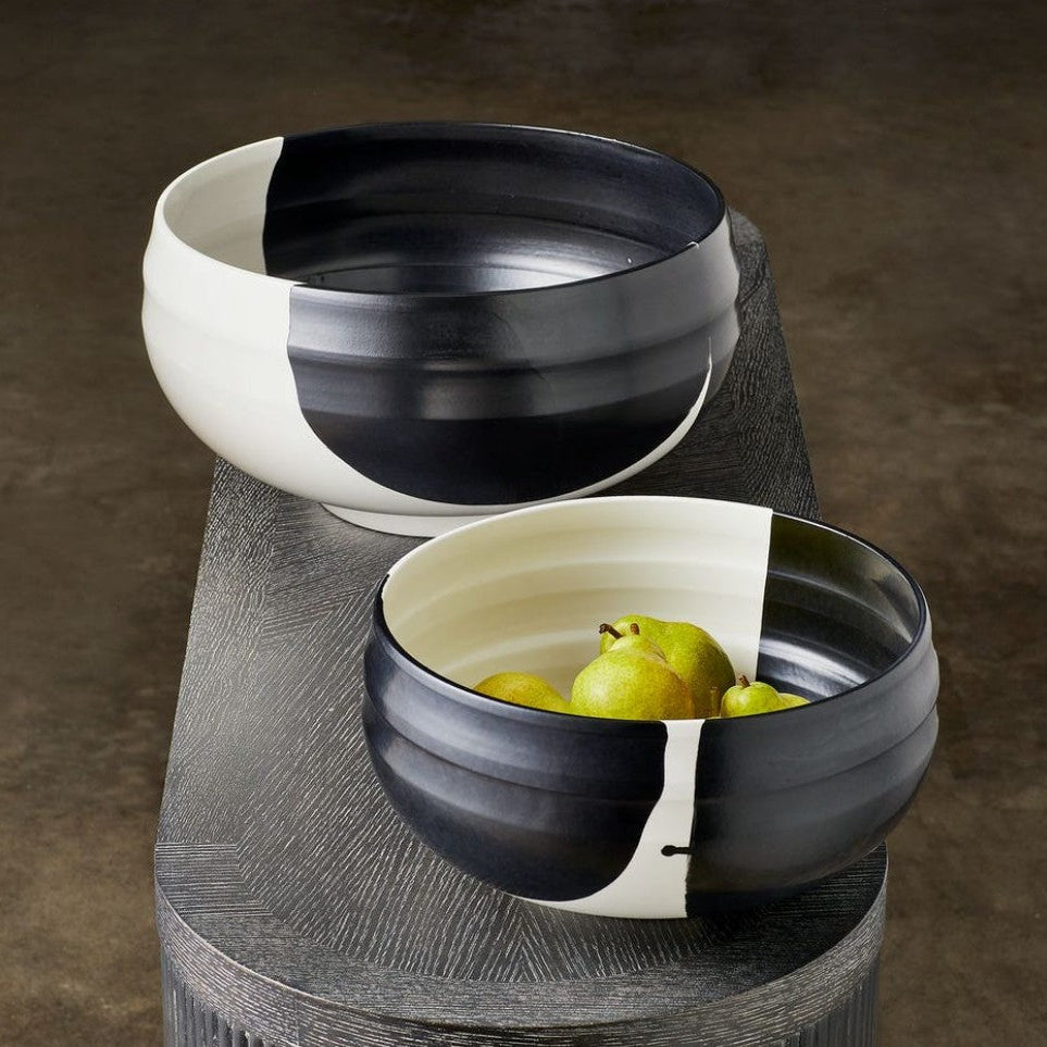 Two black and white ceramic bowls on a textured surface with pears inside one of them.