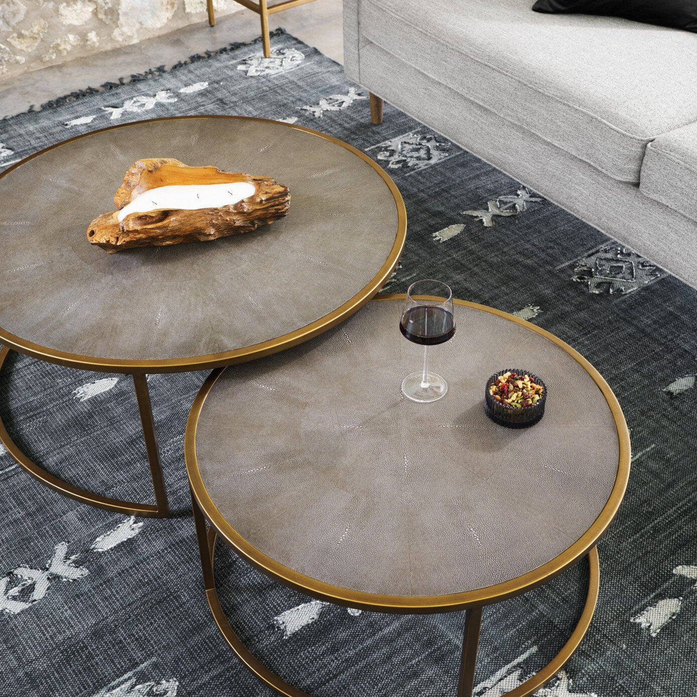 Two round shagreen nesting coffee tables with bronze-colored metal legs, placed on a grey area rug in a living room setting.