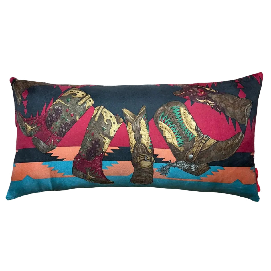 A rectangular lumbar throw pillow featuring a western-themed print of cowboy boots and a horse against a sunset landscape, shown on a light gray background.
