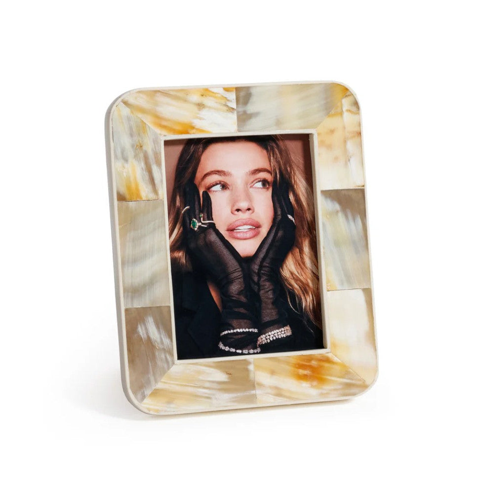 A square picture frame made of polished shell with a marbled pattern in cream, beige, and yellow tones, holding a portrait of a woman.