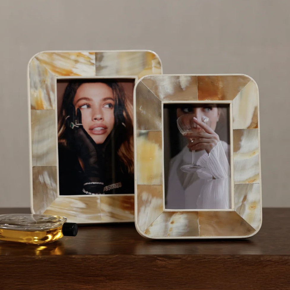 Two square photo frames with a natural mother-of-pearl shell inlay, displayed on a wooden surface against a neutral beige background.