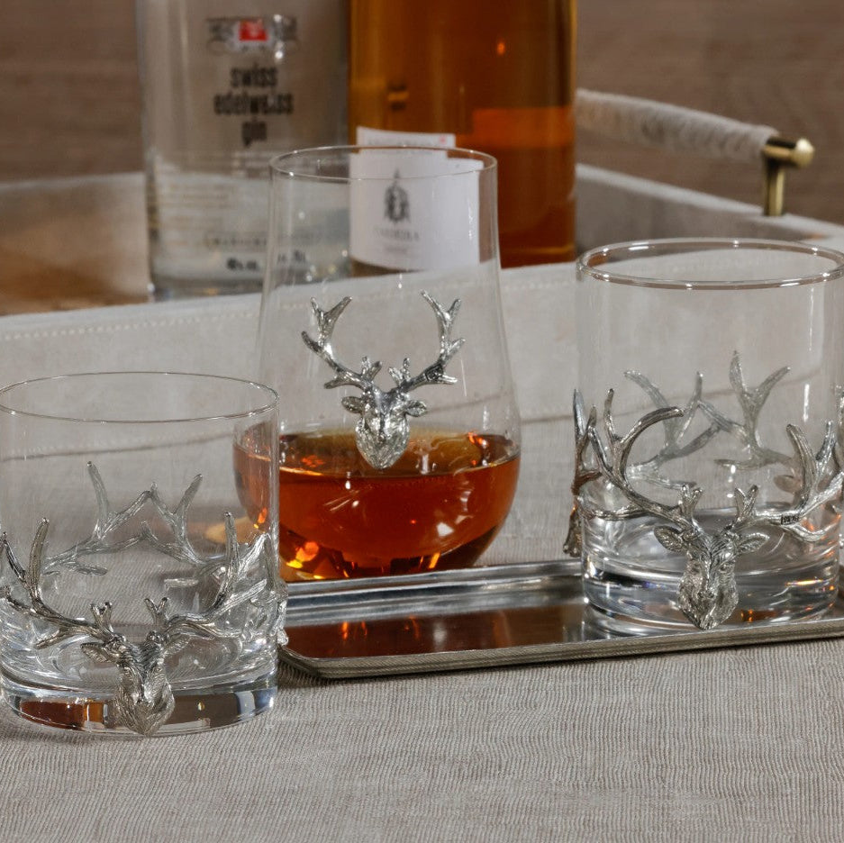 Three glasses with deer antler design on a tray with a bottle of whiskey in the background.
